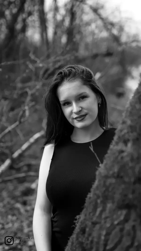 Schwarz-Weiß-Portrait einer Frau im Wald mit natürlichem Licht und sanftem Lächeln